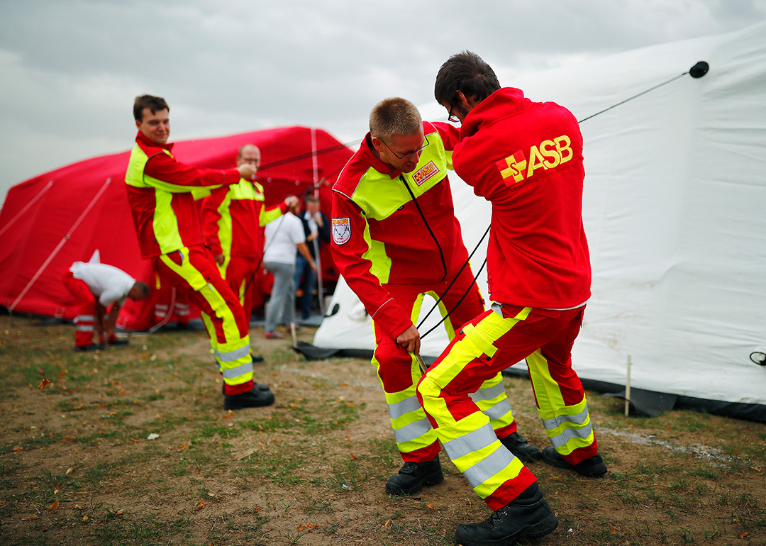 Samariter:innen in Einsatzkleidung richten per Zug an Zeltleinen Zeltunterkünfte auf.