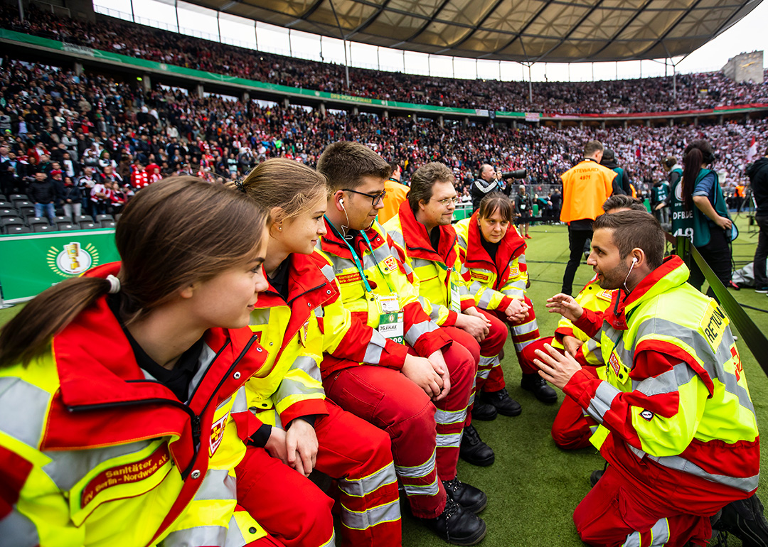 Einsatzbesprechung mit sieben Sanitäter:innen am Spielfeldrand