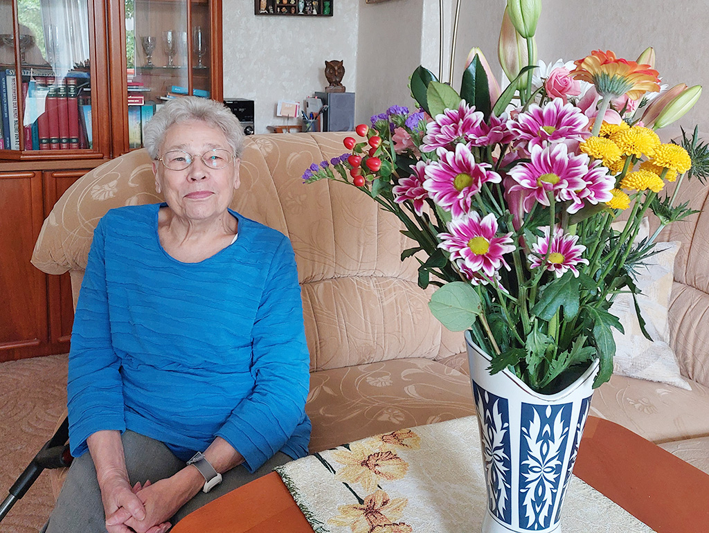 750ste Kundin mit Hausnotrufarmband auf dem Sofa neben Blumenstrauss